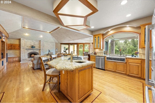 kitchen with light hardwood / wood-style flooring, stainless steel dishwasher, a brick fireplace, brick wall, and vaulted ceiling