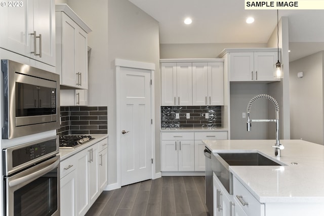 kitchen featuring appliances with stainless steel finishes, light stone counters, dark wood-type flooring, white cabinets, and hanging light fixtures