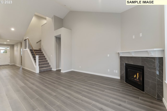 unfurnished living room featuring a tiled fireplace, high vaulted ceiling, and wood-type flooring