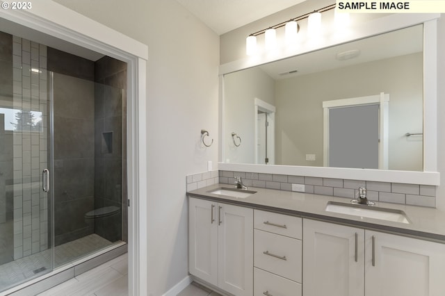 bathroom featuring vanity, a shower with shower door, and backsplash