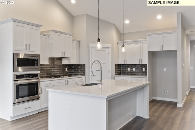 kitchen featuring appliances with stainless steel finishes, white cabinetry, a kitchen island with sink, and pendant lighting