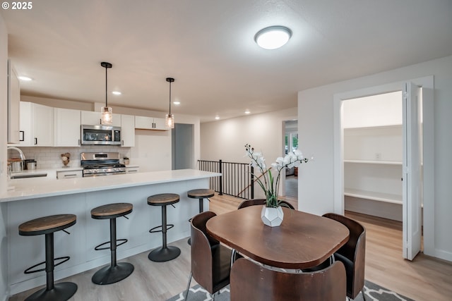 kitchen with pendant lighting, stainless steel appliances, backsplash, white cabinetry, and sink