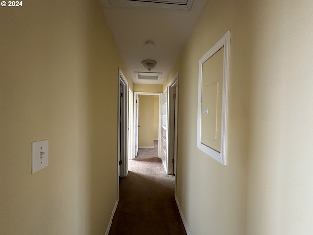 corridor featuring dark carpet and baseboards