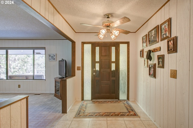 entrance foyer featuring wood walls, ceiling fan, a textured ceiling, and ornamental molding