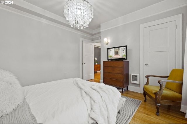 bedroom with ornamental molding, a notable chandelier, hardwood / wood-style floors, and heating unit