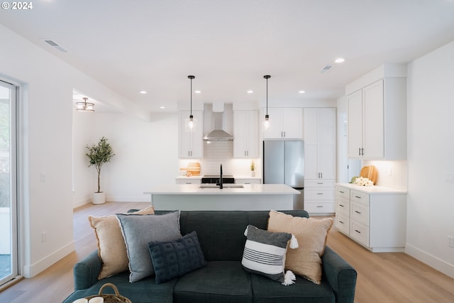 kitchen featuring a sink, wall chimney range hood, light wood-type flooring, freestanding refrigerator, and tasteful backsplash