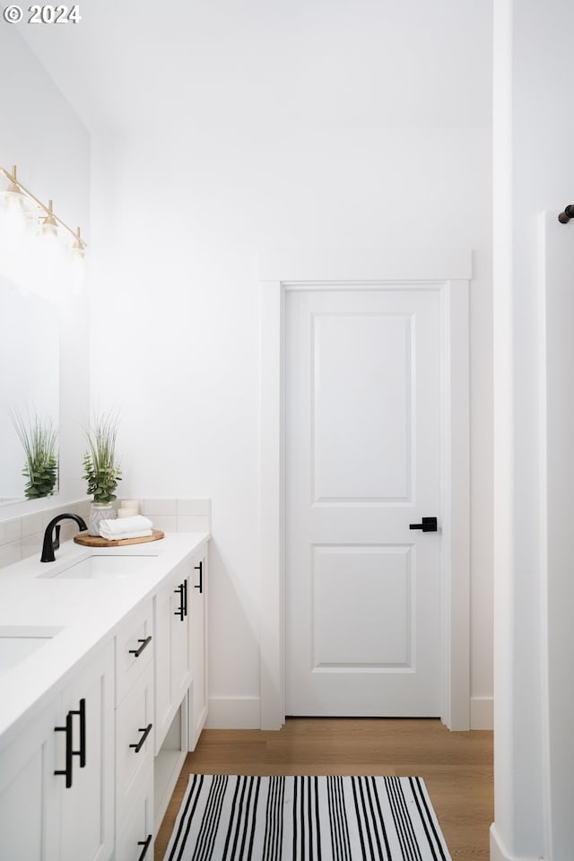 full bath with double vanity, baseboards, a sink, and wood finished floors