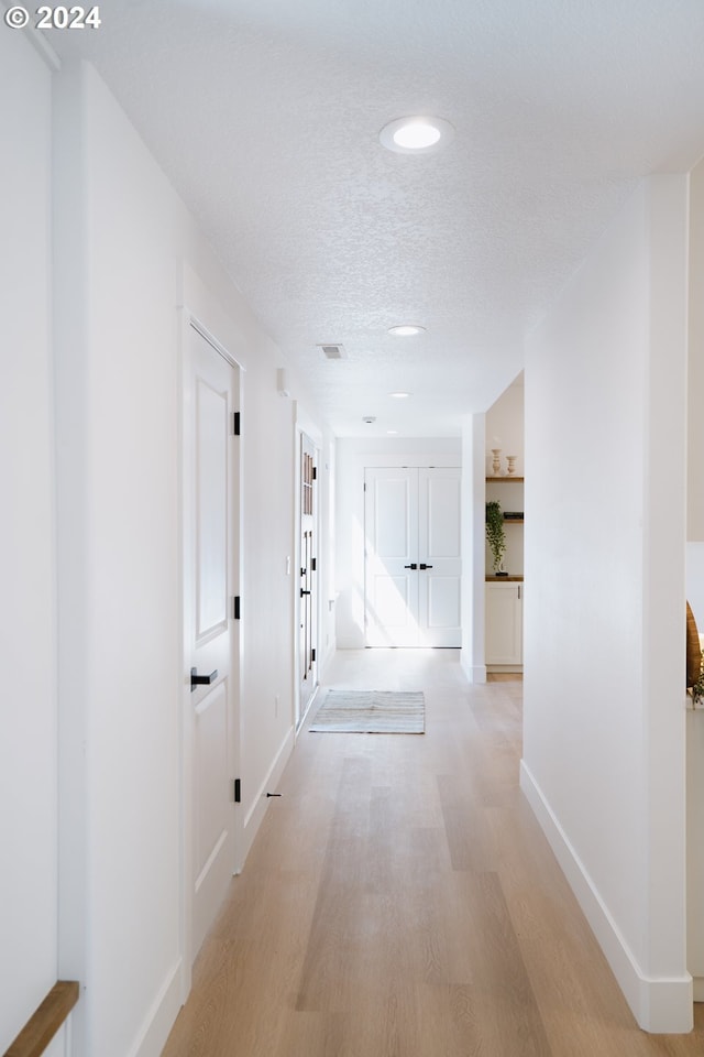 hallway featuring light wood finished floors, baseboards, and a textured ceiling