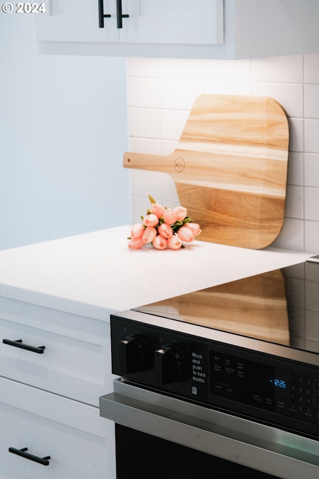 details featuring light countertops, tasteful backsplash, range, and white cabinets