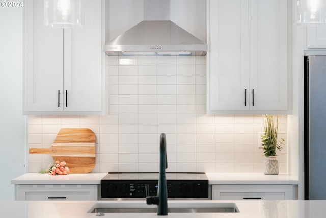 kitchen with light countertops, backsplash, freestanding refrigerator, a sink, and wall chimney exhaust hood