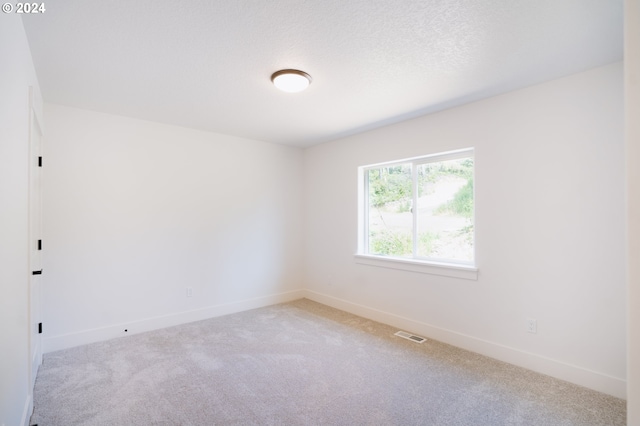 empty room featuring a textured ceiling, carpet, visible vents, and baseboards