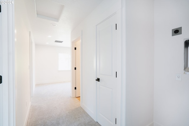 hall with attic access, light colored carpet, visible vents, and baseboards