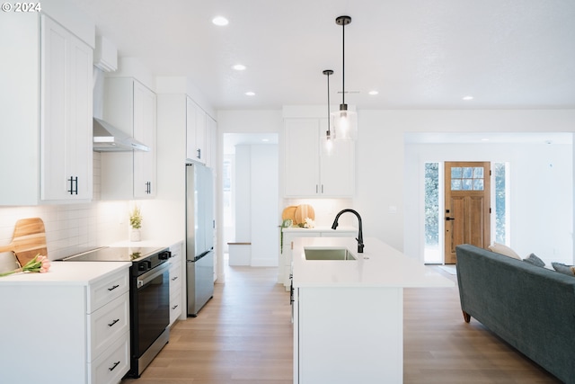 kitchen with electric stove, light countertops, freestanding refrigerator, a sink, and an island with sink