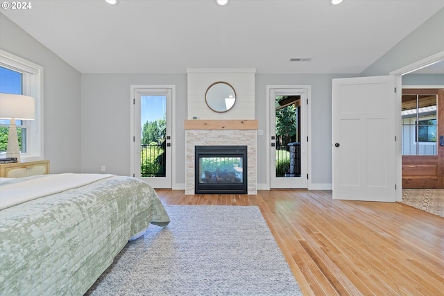 unfurnished bedroom featuring access to exterior, light wood-type flooring, a stone fireplace, and multiple windows