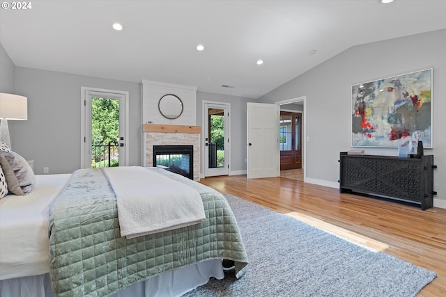 bedroom featuring access to outside, light hardwood / wood-style floors, a stone fireplace, and lofted ceiling