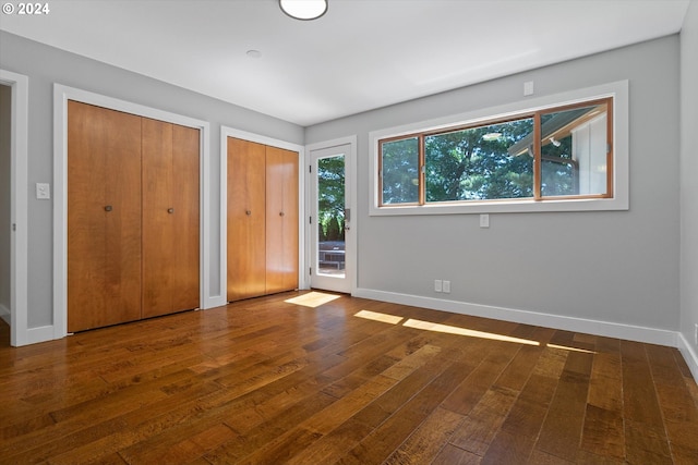 unfurnished bedroom with two closets and dark wood-type flooring