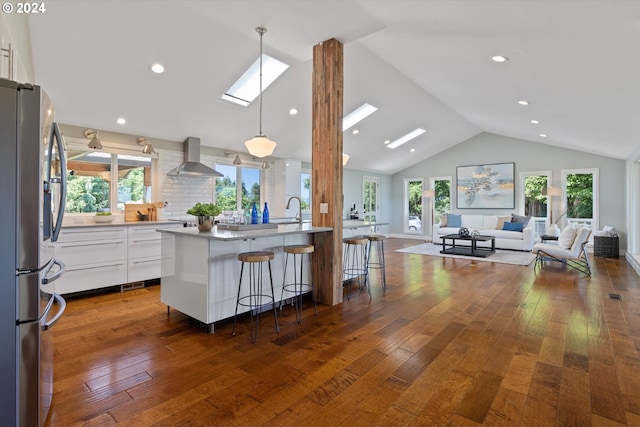 kitchen featuring stainless steel refrigerator, dark wood-type flooring, wall chimney range hood, a breakfast bar area, and white cabinets