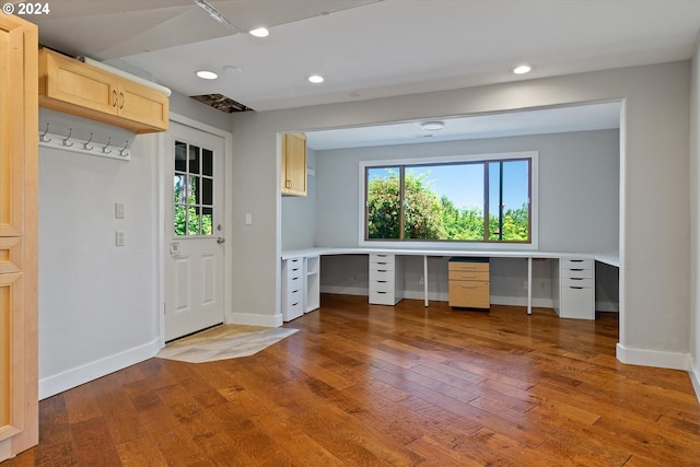 unfurnished office featuring hardwood / wood-style floors and built in desk