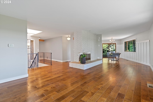 unfurnished living room with an inviting chandelier, wood-type flooring, and a brick fireplace