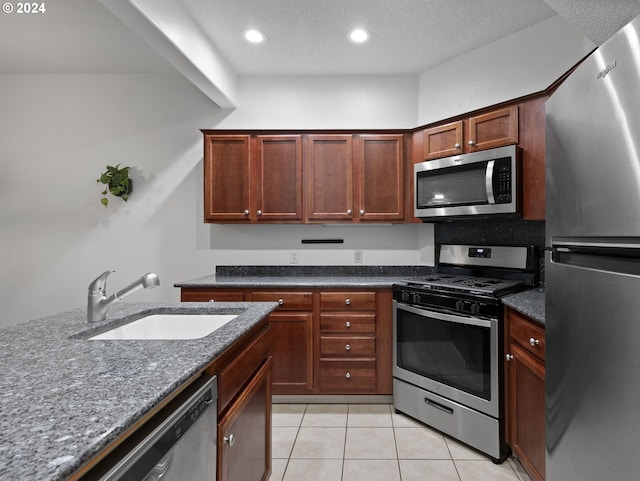 kitchen featuring light tile patterned floors, stainless steel appliances, dark stone counters, and sink