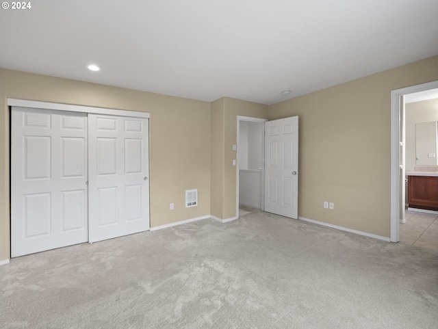 unfurnished bedroom with ensuite bathroom, a closet, and light carpet