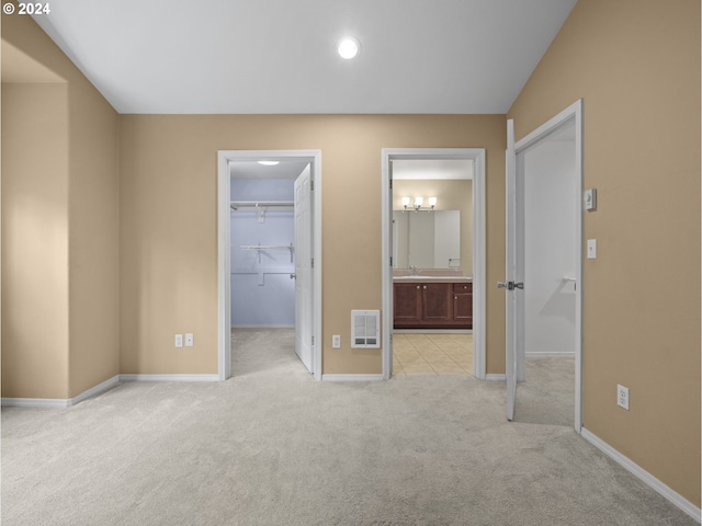 unfurnished bedroom with sink, ensuite bath, a spacious closet, light colored carpet, and a closet