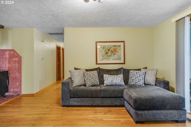 living room featuring a brick fireplace, light hardwood / wood-style floors, and a textured ceiling