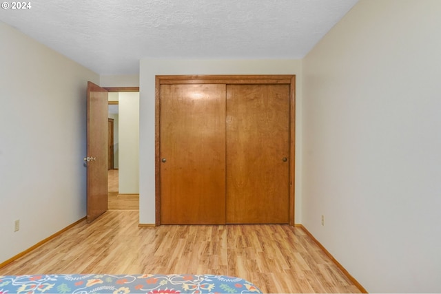 unfurnished bedroom featuring light wood-type flooring, a textured ceiling, and a closet