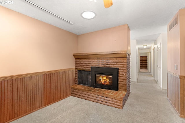 unfurnished living room featuring light carpet, wood walls, a textured ceiling, and a brick fireplace