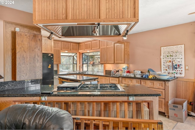 kitchen with kitchen peninsula, stainless steel gas stovetop, light tile patterned floors, light brown cabinets, and black refrigerator