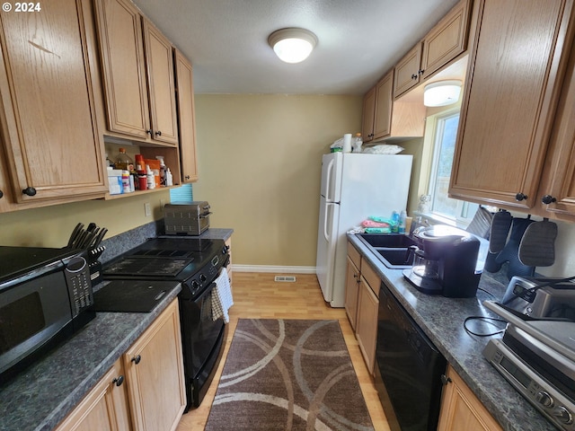 kitchen featuring light wood-type flooring, black appliances, sink, and dark stone countertops