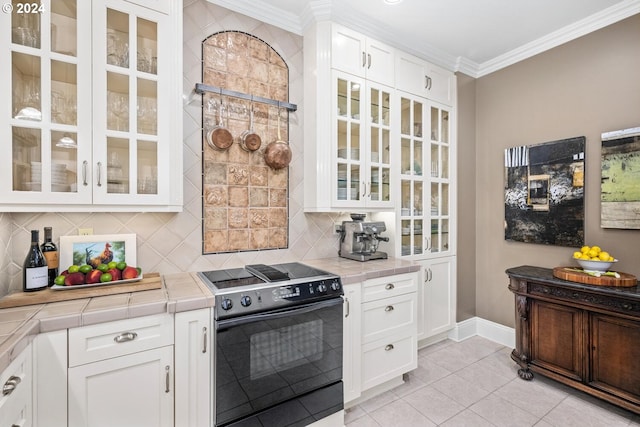 kitchen with tile counters, black range with electric cooktop, ornamental molding, and white cabinets