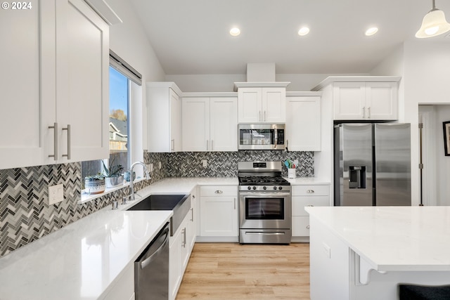 kitchen with stainless steel appliances, hanging light fixtures, white cabinetry, and light wood-type flooring