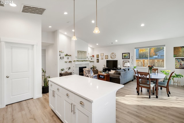 kitchen with hanging light fixtures, a kitchen island, white cabinetry, a fireplace, and light hardwood / wood-style flooring