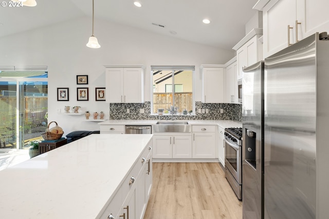 kitchen with lofted ceiling, light hardwood / wood-style floors, decorative light fixtures, and appliances with stainless steel finishes