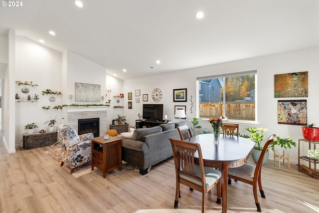 dining area with vaulted ceiling, a tile fireplace, and light hardwood / wood-style flooring