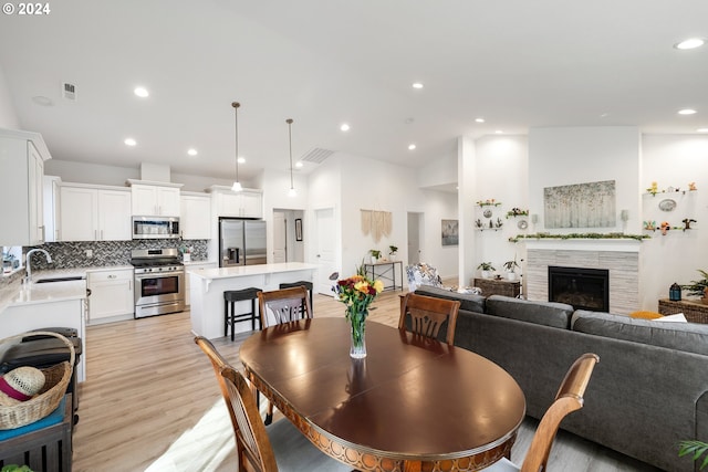 dining area with a tile fireplace, sink, light wood-type flooring, and lofted ceiling