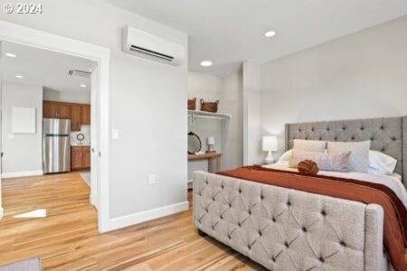 bedroom featuring a wall mounted AC, light hardwood / wood-style floors, and stainless steel fridge