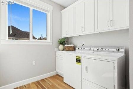 washroom with light wood-type flooring, washing machine and dryer, and cabinets