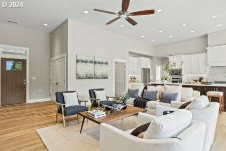 living room featuring ceiling fan, light hardwood / wood-style flooring, and a towering ceiling