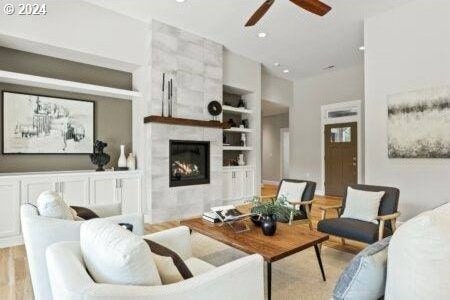 living room with ceiling fan, a fireplace, built in shelves, and light hardwood / wood-style flooring