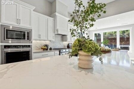 kitchen featuring appliances with stainless steel finishes, backsplash, white cabinetry, and light stone countertops