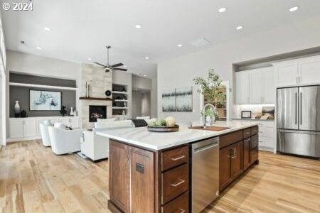 kitchen featuring a center island with sink, light wood-type flooring, appliances with stainless steel finishes, a large fireplace, and sink