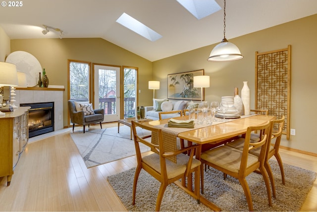 dining room featuring a tiled fireplace, vaulted ceiling with skylight, light hardwood / wood-style floors, and track lighting