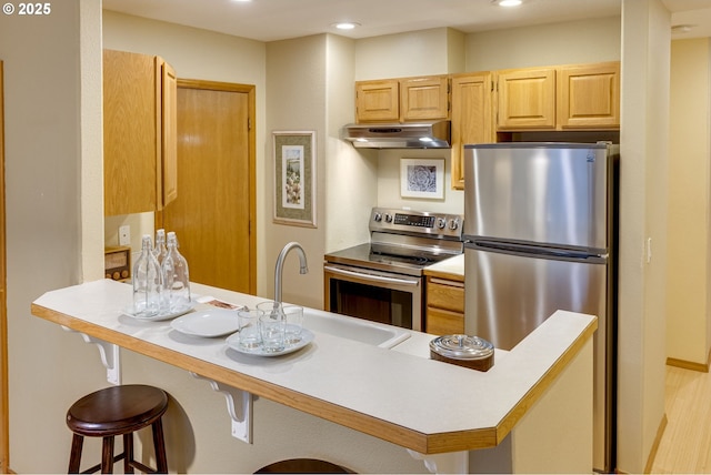 kitchen with a kitchen bar, appliances with stainless steel finishes, kitchen peninsula, light brown cabinets, and light hardwood / wood-style floors