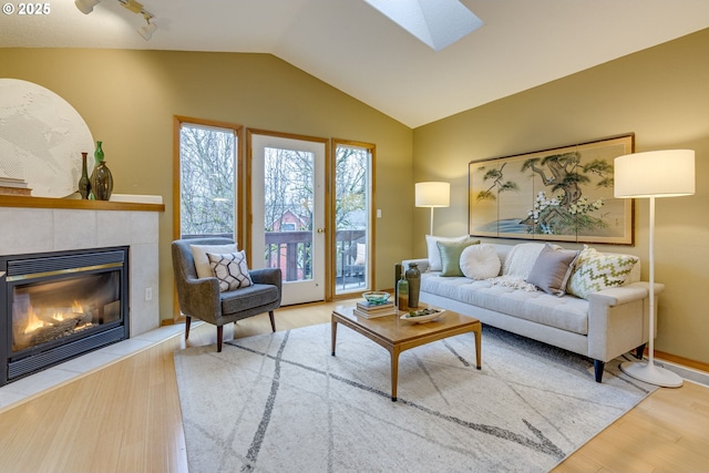 living room with a tile fireplace, light hardwood / wood-style floors, and lofted ceiling with skylight