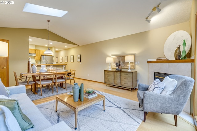 living room with a fireplace, light wood-type flooring, rail lighting, and vaulted ceiling with skylight