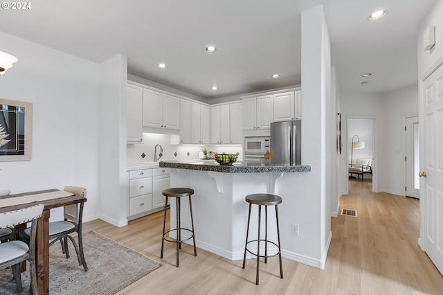 kitchen with stainless steel fridge, white microwave, light hardwood / wood-style floors, white cabinetry, and a breakfast bar area