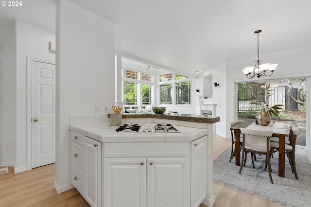 kitchen with white cabinetry, white gas cooktop, light hardwood / wood-style flooring, kitchen peninsula, and ceiling fan with notable chandelier