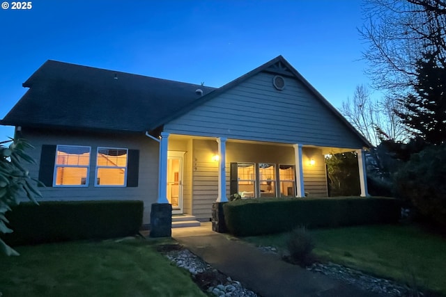 back house at dusk with a lawn and covered porch